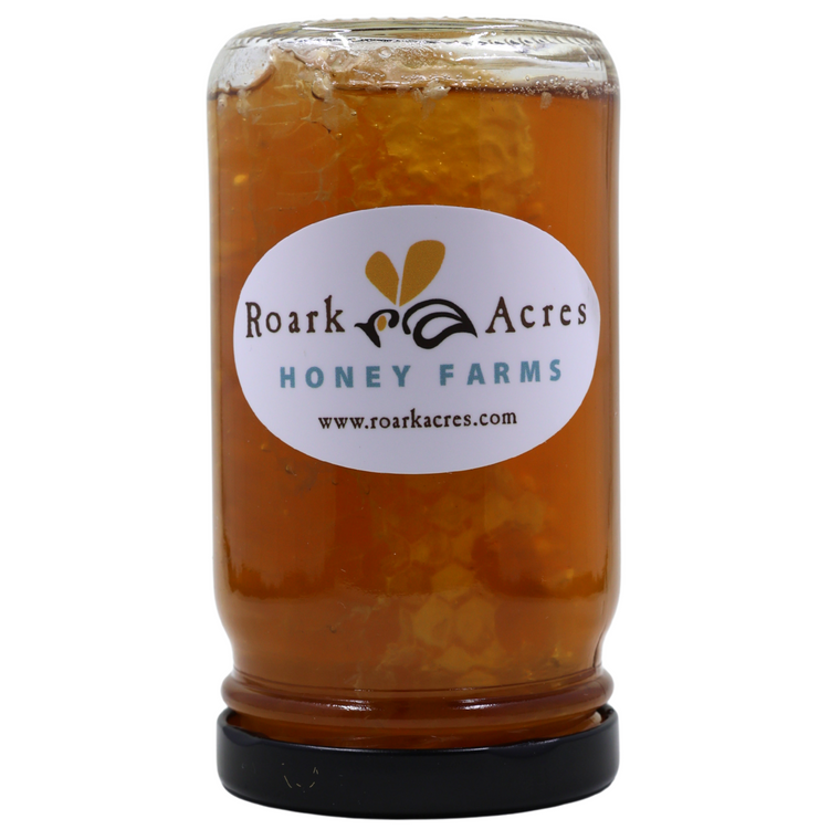 Half pint jar of honey and honeycomb with a label reading "Roark Acres Honey Farms www.roarkacres.com" on a white background.